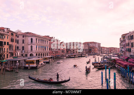 Colorful pink sunset  at dusk over the Grand Canal, Venice, Italy as viewed from Rialto Bridge over Riva del Vin with gondolas and boat traffic  and t Stock Photo