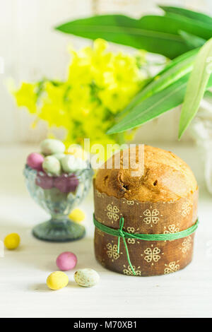 Home Baked Easter Sweet Cake Panettone in Paper Form Tied with Twine. Multicolored Speckled Chocolate Candy Eggs in Crystal Egg Cup Scattered on White Stock Photo