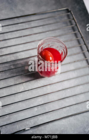Red colored eggs with red tint are displayed on a metallic grate  top view over a gray concrete background Stock Photo