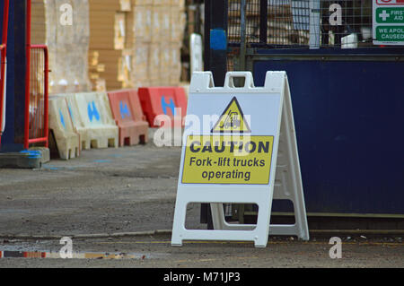 Workplace safety for building sites - caution fork- lift trucks operating in yellow on a black background placed next to entrance gate to site Stock Photo