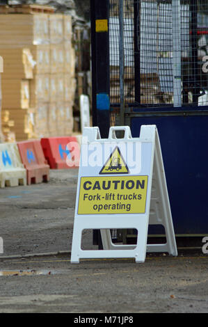 Workplace safety for building sites - caution fork- lift trucks operating in yellow on a black background placed next to entrance gate to site Stock Photo