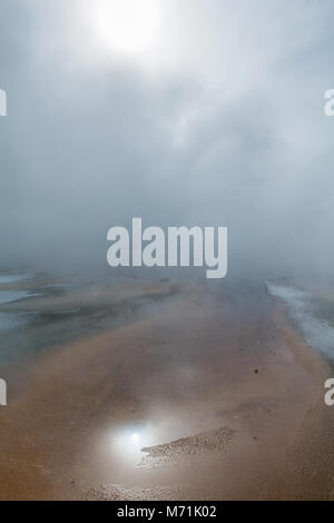 The sun reflects weakly through the mist rising from a geyser pool in Yellowstone National Park. Stock Photo