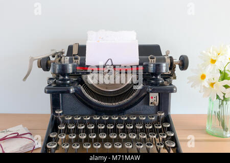 Antique typewriter with blank paper in the carriage on a wooden table with flowers and a bundle of note cards tied with a string Stock Photo
