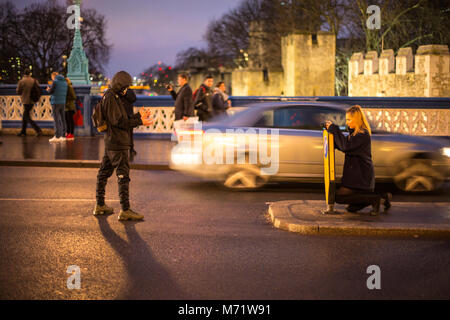 Two young people in traffic taking photographs at Tower Bridge, London, at night. Stock Photo