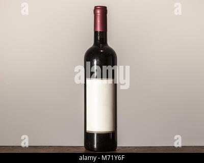 Isolated vintage bottle of red wine with a white label standing on an old wooden table   Picture of a bottle of red wine, isolated in front of a white Stock Photo