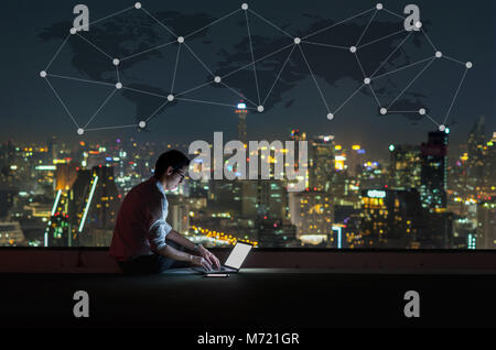 Asian businessman sitting and using the laptop with Network graphic over the world map and cityscape background at night time, Business success and te Stock Photo