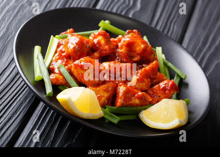 Spicy chicken pieces in red sauce with green onions and lemon close-up on a plate on a table. horizontal Stock Photo