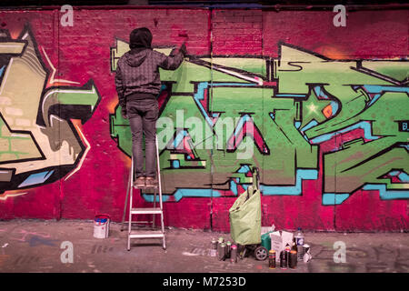 Man standing on a ladder painting graffiti, at Leake Street tunnel, London, near Waterloo Station. Stock Photo