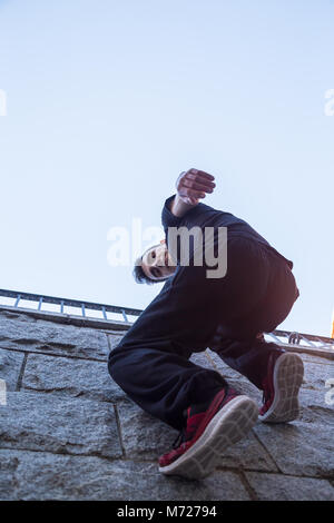 Young man hanging on wall and trying to climb up while doing parkour. Stock Photo