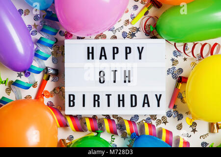 Happy 8th birthday celebration message on a lightbox with balloons and confetti Stock Photo