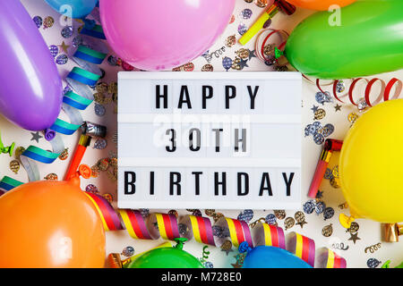 Happy 30th birthday celebration message on a lightbox with balloons and confetti Stock Photo