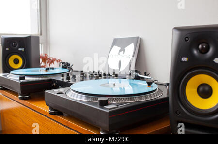 A DJ set-up with two turntables, mixer and monitor speaker. Wu-Tang manual book leaning on wall. All set up on wooden folded table. Red plant in backg Stock Photo