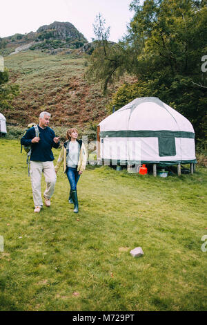 Senior couple are leaving the yurt they have been camping in to go for a hike around the Lake District. Stock Photo