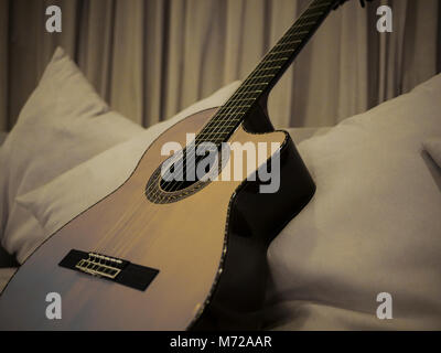 A monochrome picture of a lovely nylon string guitar resting on a white couch Stock Photo