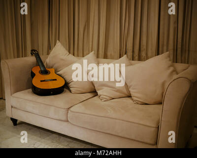 A guitar resting on a sofa in the living room after being used in a recording Stock Photo