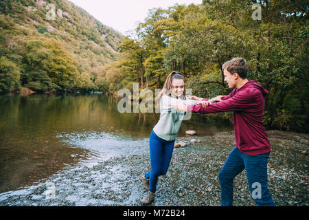 Teenage boy is being pushed away by his sister as he is trying to push her in to a lake they have found while hiking. Stock Photo