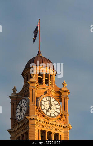 The clock tower with its bronze dome and Australian flag atop bathes in morning sun at Sydney's iconic Central Station, NSW, Australia Stock Photo