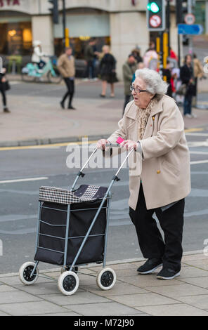 Elderly lady pushing a wheeled shopping trolley at shops in the UK. Stock Photo