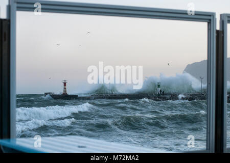 Fishermen braving enormous waves that are seen here crashing up against the breakwater of Kalk Bay harbour in Cape Town, South Africa. The scene is fr