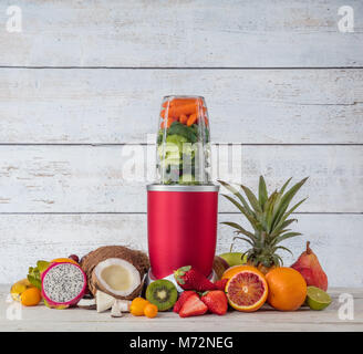 Smoothie maker mixer with pieces of fruit ingredients, placed in wooden interior. Healthy drink and lifestyle Stock Photo