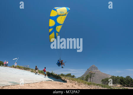 Tandem paraglider launching off the slopes of Signal Hill in Cape Town. Lion’s Head and Table Mountain can be seen in the background. Stock Photo