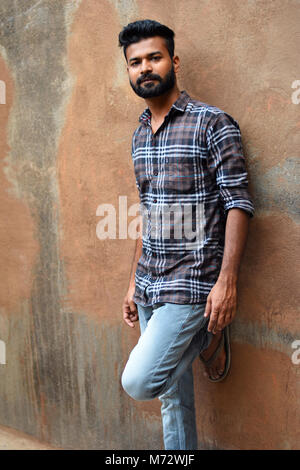Male model looking at camera with leg against wall. Mumbai, Maharashtra Stock Photo