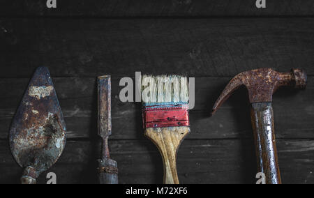 old and rusty construction or carpentry tools on wooden table; hacksaw, paint brush, hammer, chisel, mortar Stock Photo