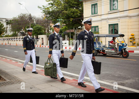 Three young officers of the Thai army walk in single line on a street, with a tuk tuk passing by in the background, the day after the Royal Cremation Stock Photo