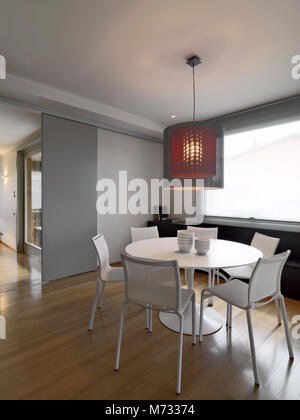 interiors shots of a modern dining room in the foreground the modern white round dining with white chairs table the floor is made of wood Stock Photo