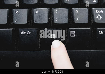 Brazil - March 02, 2018: Finger pressing the Windows key from a dusty black keyboard. Stock Photo