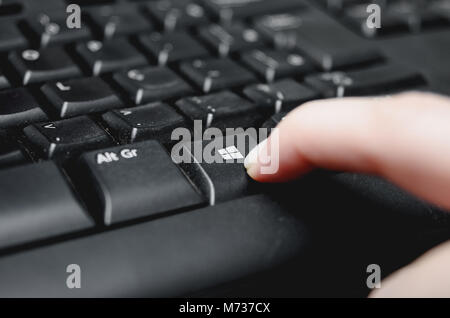 Brazil - March 02, 2018: Finger pressing the Windows key from a dusty black keyboard. Stock Photo