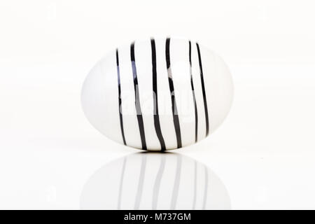 one striped black and white Easter egg on white with reflection in surface Stock Photo