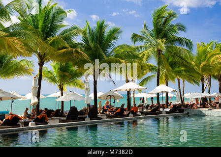 beach chairs with white umbrellas near infinity pool among palm trees and on the edge of the sea Stock Photo