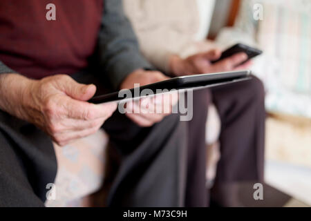 closeup of an old caucasian man using a tablet and an old caucasian man using a smartphone, sitting both in a couch Stock Photo