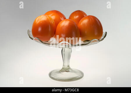 Glass bowl with kaki fruits (persimmons, sharon) on a gray background, studio Stock Photo