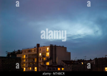 Night is falling on a residential building with illuminated rooms in a popular district under a dark blue sky. Stock Photo