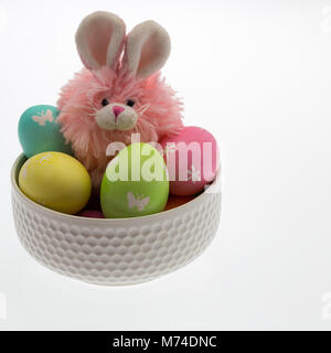 Pink easter bunny, yellow chick and several hand dyed eggs with pastel coloured paper shred in a white bowl conveying an easter theme for children. Stock Photo