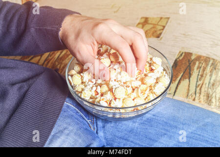 A man with a bowl of popcorn in his hand is watching TV on the sofa Stock Photo