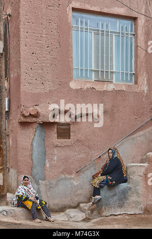 Abyaneh, Iran - April 26, 2017: two Iranian women in hijabs sit on the stairs in the countryside in the mountains. Stock Photo