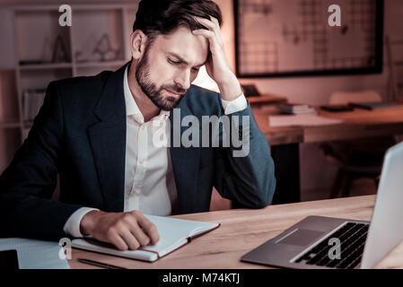 Upset deep man supporting his head sitting by the table. Stock Photo