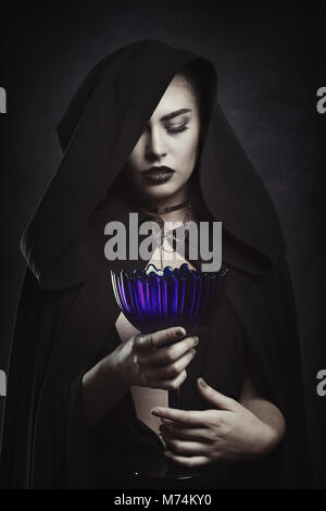 Beautiful vampire with a ritual cup. Hooded figure Stock Photo