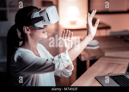 Amazed interested woman sitting and using VR glasses. Stock Photo