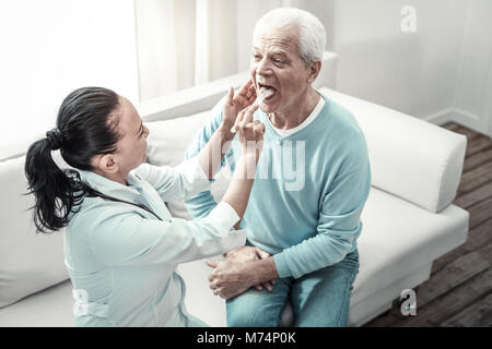 Old serious man looking at the nurse showing his tongue. Stock Photo