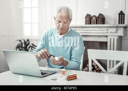 Serious concentrated man sitting and taking the pills. Stock Photo