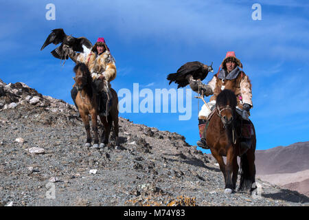 Kazakh brothers out hunting in the Altai Mountains of western Mongolia riding on their horses with their golden eagles. Stock Photo