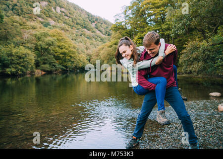 Teenage boy has his sister in a piggy back hold and is pretending to throw her in to a lake while they are out hiking. Stock Photo