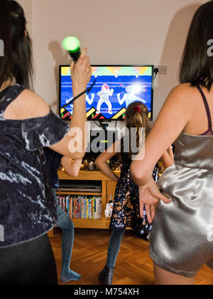 Vertical portrait of four girls dancing and singing together on their games console. Stock Photo