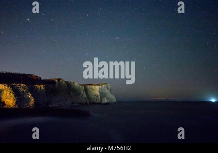 Chalk cliffs of Seaford Head under starry sky, with light from Newhaven to Dieppe Ferry on the horizon. Stock Photo