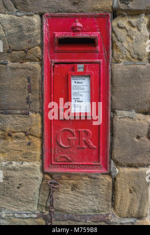 Old red wall mounted British Post Ofice Post Box on a Sandstone wall, featuring Crown and Time table Stock Photo