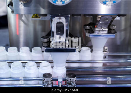 medicine pill capsules are filling in the white plastic bottle on production line machine conveyor at the medical factory. Stock Photo